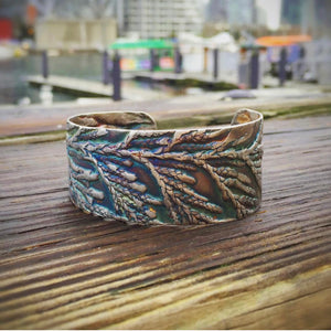 close up shot of sterling silver west coast jewelry cedar cuff bracelet with vancouver skyline in the background