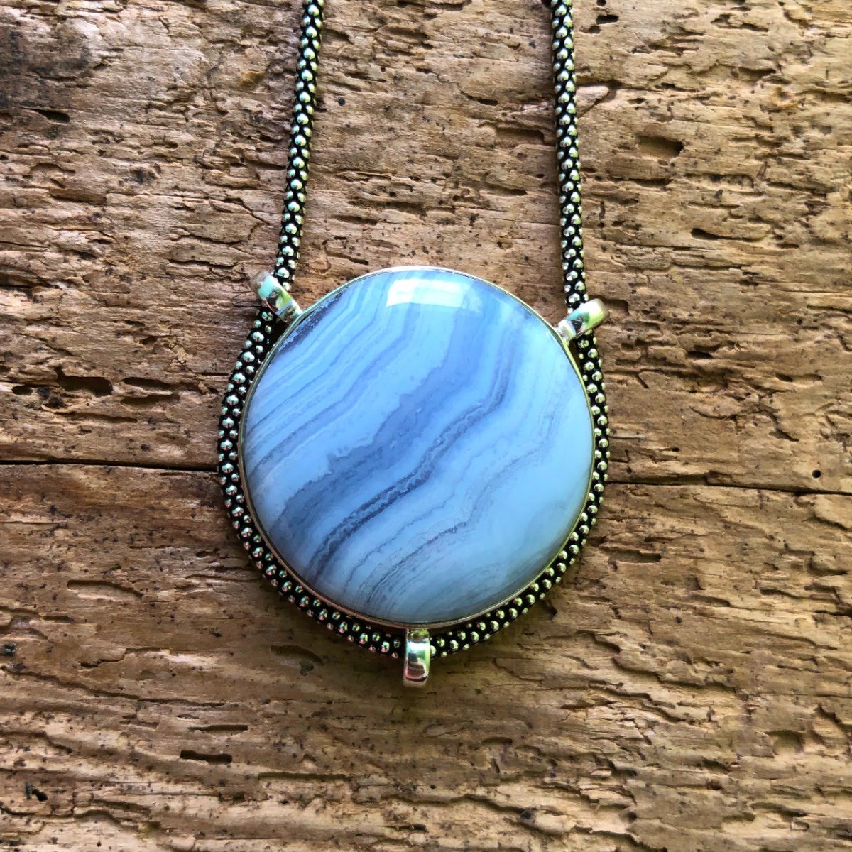 Strikingly good quality circular Blue Lace Agate Pendant with oxidized sterling silver chain on driftwood background