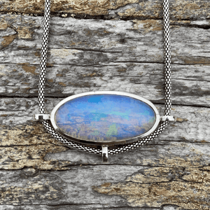 blue opal pendant set in sterling silver smooth oval shape on a piece of driftwood