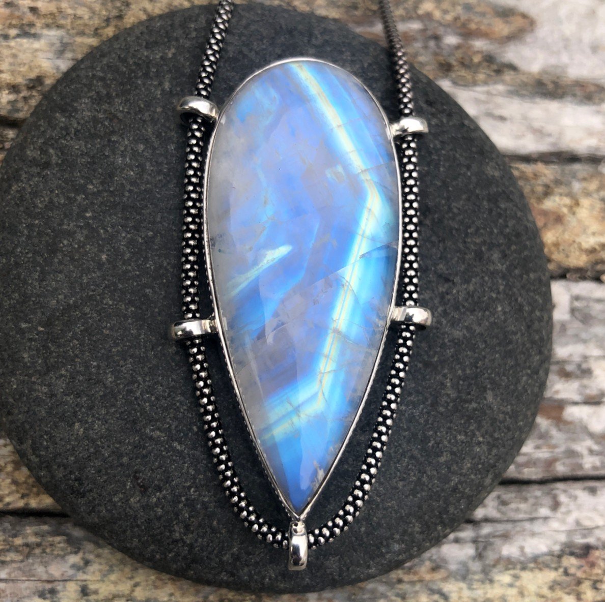 handmade moonstone pendant with lots of blue and a big octagon shape flash on a dark stone background