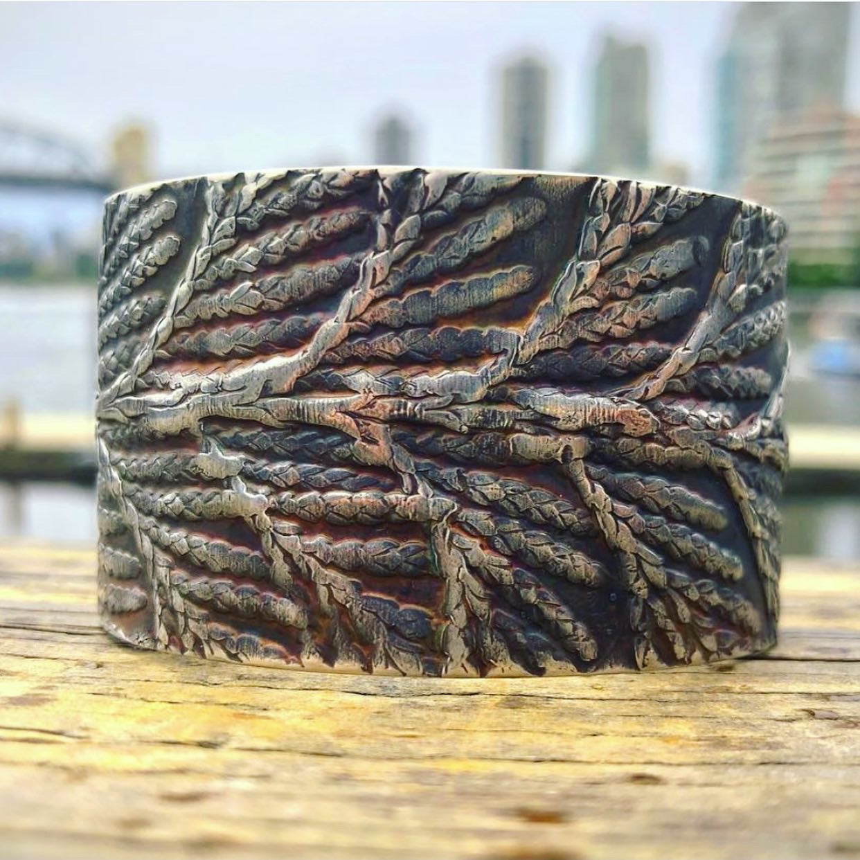 close up shot of sterling silver west coast jewelry cedar cuff bracelet with vancouver skyline in the background