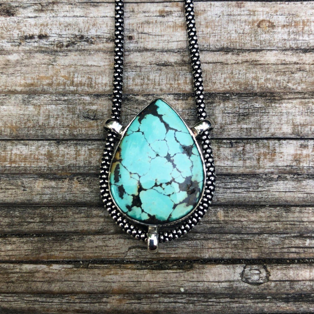 authentic turquoise horizontal teardrop shaped pendant on unique Sterling Silver setting. on weathered driftwood background. Sterling Silver Chain