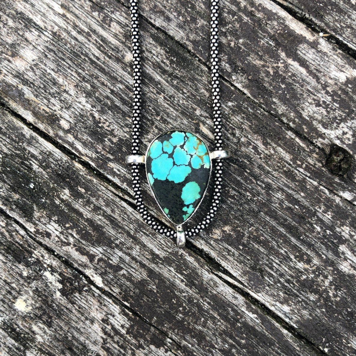 authentic turquoise upside down tear shaped pendant on unique setting weathered driftwood background. sterling silver oxidized chain